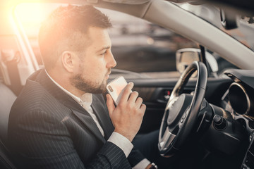 Handsome caucasian businessman driver inside in vehicle  with coffee and gadget and check mail and talking with partners