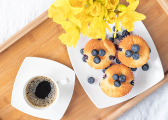Wooden tray on the bed. Blueberry cupcakes and cup of coffee. Perfect breakfast and start of the day. Top view