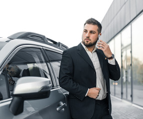 Handsome businessman with smartphone near vehicle on office parking