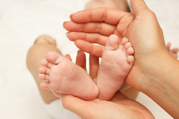 Obraz na płótnie Canvas Hands of woman holds baby feet, blurred background