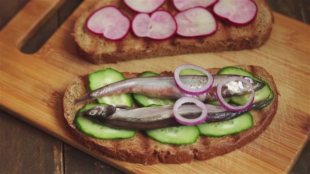 place red onion rings on sandwich with salted  fish sardines capelin cucumber