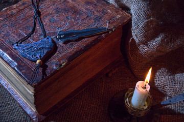 Naklejka premium Old book and rough cloth. The musical instrument of the harbor lies on the book. The plate with the image of the head of a wolf. A bright candle burns. The concept of occultism and magic.