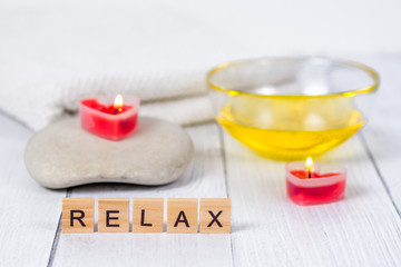 Fototapeta na wymiar The concept of a Spa on Valentine's Day. Burn red heart-shaped candles, stones, massage oil, word relax and white towel on wooden background. Relaxation and wellness care. Bath procedure, cosmetology