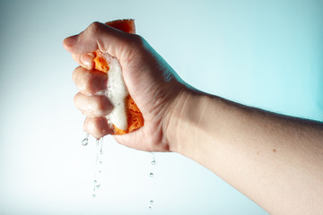 man’s hand squeezes a sponge for washing with water, washing with it and drops fall down concept on a light background copy space close up