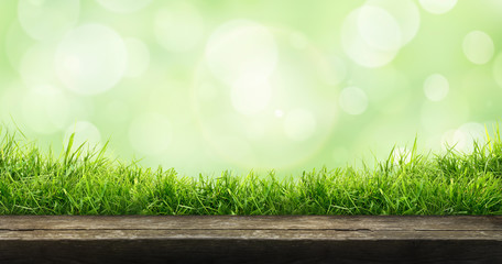 A fresh spring sunny garden background of green grass and blurred foliage bokeh with a wooden table to place cut out products on.