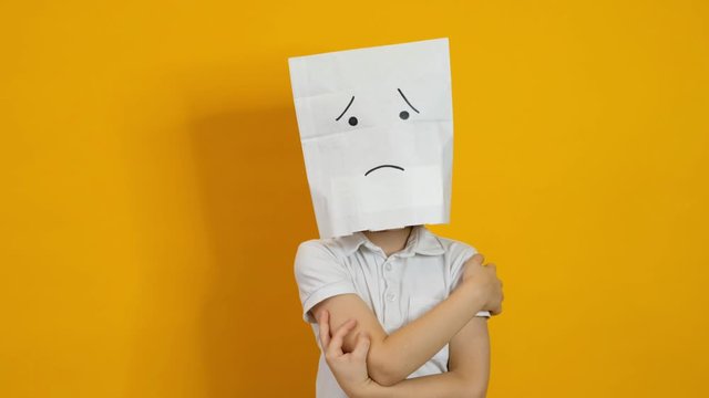Little boy with a bag on his head - sad, dissapointed face on yellow background