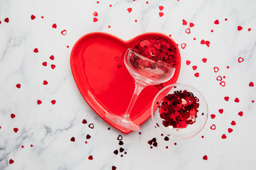 Valentine's dinner background. Red heart plate with champagne glass and confetti