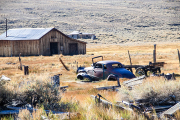 Old wooden building in ghost town and car remains