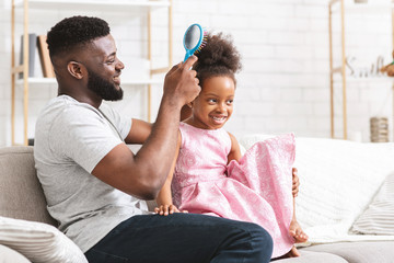Happy black dad brushing his beautiful little daughter