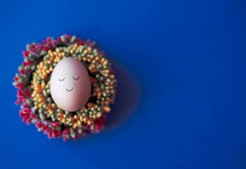 An egg with a cute painted face on a classic blue background. The classic blue flower is the trendy color of the year.