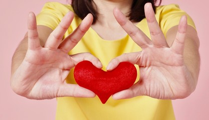 woman in yellow blouse holding a small red heart on two hands on the pink background