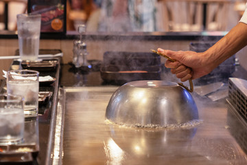 cooking on a Japanese frying pan, the frying surface of Tepanyaki. The cook has covered the cooking...