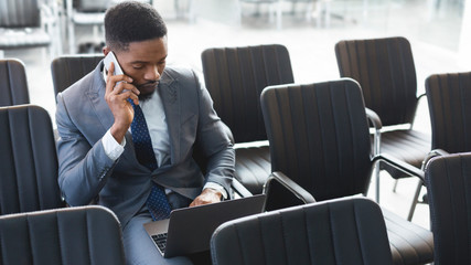 Concentrated afro businessman working on laptop in empty conference hall