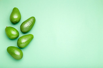 Fresh ripe organic green avocados on color background, top view summer food concept. Minimal flat lay style avocado whole fruit on mint green background with copy space for text.