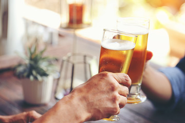 Two young men colliding with two glass of beer to celebrate their success.