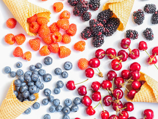 Mix of berries with waffle cones on a white background. Top view summer berries, blueberry, blackberry, raspberry and cherry