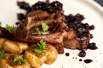 Lamb ribs with baked potatoes on a white plate, close-up.