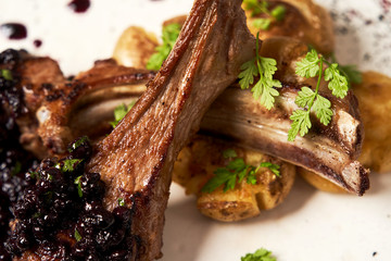 Lamb ribs with baked potatoes on a white plate, close-up.