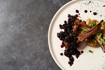 Lamb ribs with baked potatoes on a white plate, close-up.