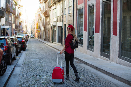 Traveler woman walking in old european town with red suitcase.