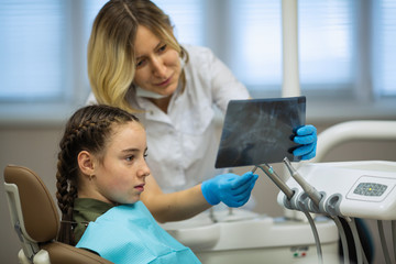 Dentist woman shows an x-ray to a little girl patient in medical dental clinic.