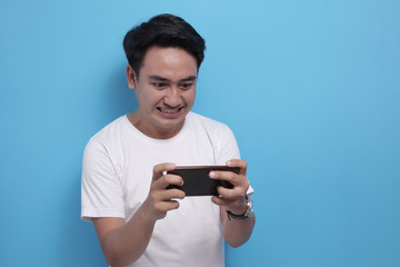 Funny Young Asian Guy Playing Games on Tablet Smart Phone