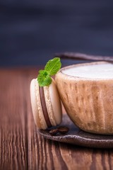 Coffee cappuccino, vanilla bean and chocolate macaroon or macaron with mint leaf on dark wooden background