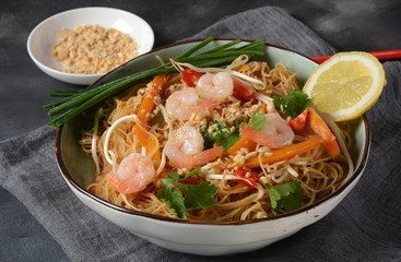 Pad Thai- traditional Thai dish with stir fried rice noodles, shrimps and vegetables on a dark background, copy space