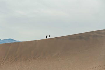 Fototapeta na wymiar Couple is walking on the edge of the great Sand dunes in Death Valley, California.