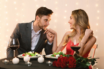Handsome man kissing hand of his girlfriend while dining in restaurant