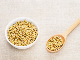Spice coriander (Coriandrum sativum) seeds in ceramic bowl and wooden spoon on beige fabric background. Healthy eating concept