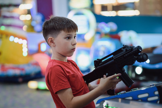 Technology, gaming, entertainment and people concept. Boy playing automatic toy gun on playground at shopping mall.