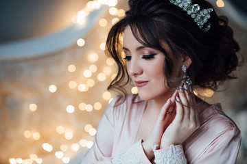 Portrait of young girl at marriage day. Beauty woman with wedding hairstyle and makeup. Bride fashion. Woman in robe, perfect skin. Magical atmosphere. The bride touches the earrings.