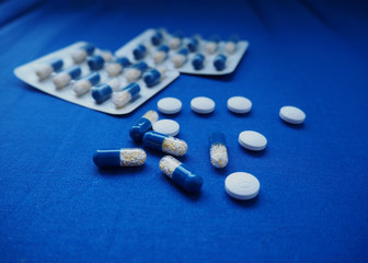 Blue and white with yellow medical pills and tablets on a blue textile background.