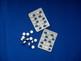 Blue and white with yellow medicine pills and tablets on blue crumpled fabric background top view with copy space. Medical banner template.