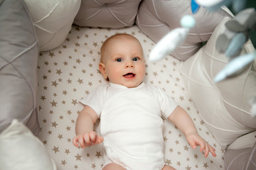 baby boy 5 months old in a white bodysuit lying in a crib top view,textiles for children's room