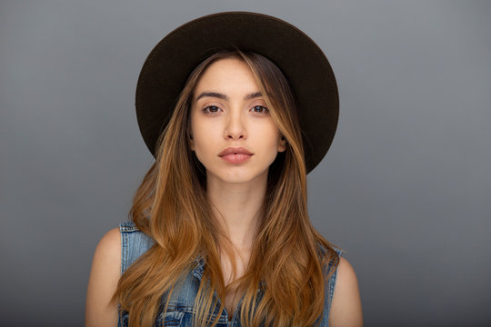 Cheerful hipster girl in stylish hat and denim vest posing at grey copy space wall for your content.