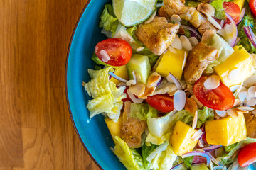 Close up shot of a mango salad with roasted chicken, lettuce, red onion and lime