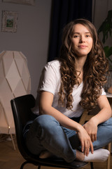 Curly hair girl in casual clothes sitting on chair at home