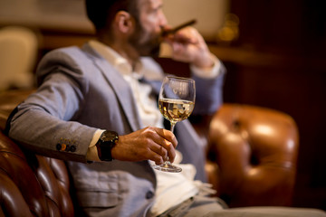 Young man tasting white wine and smoking cigar