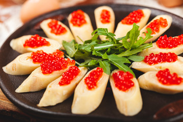 Rolled crepes (pancakes, blini) with red caviar served with arugula on black plate.