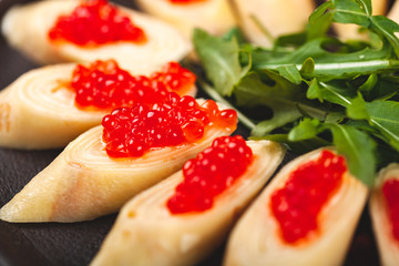 Rolled crepes (pancakes, blini) with red caviar served with arugula on black plate.