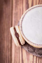 Cappuccino with white milk foam and coffee macaroon or macaron on wooden background, copy space