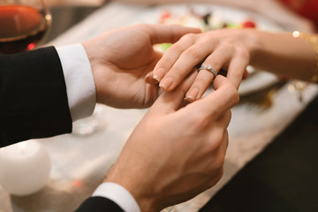 Man Putting Engagement Ring On Girlfriend's Hand During Dinner In Restaurant