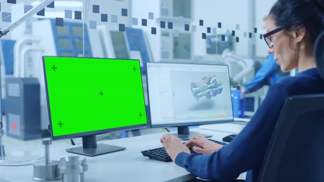 Industrial Female Engineer Working on a Personal Computer, Two Monitor Screens Show Green Mock-up Screen, CAD Software with 3D Prototype of New Electric Engine. Modern Factory with High-Tech Machinery