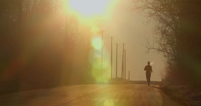 The guy is running down the hill on the road at dawn. Cold weather. 4K