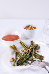 Asparagus roasted in olive oil with crushed walnuts and sauce on a white plate. Vegetarian food.