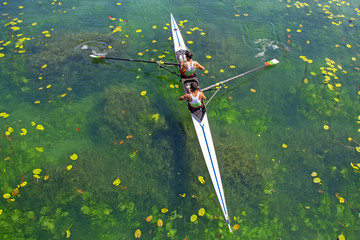 Two young athletes rowing team on green lake