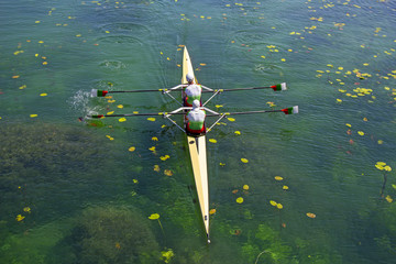 Two young athletes rowing team on green lake