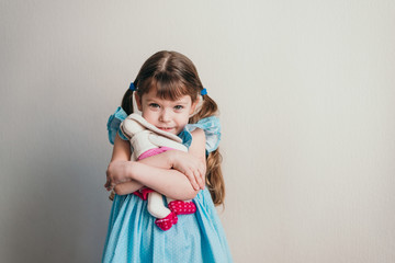 Little girl in blue dress looks at camera and hugs her toy